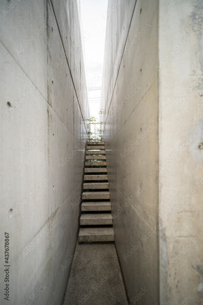 Narrow exposed concrete stair and lighting at the end of small corridor express to minimal style of architecture.