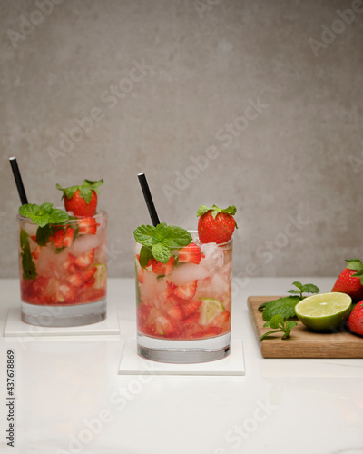 Strawberry mojito cocktails with strawberries, lime, mint and ice in glass on gray background. Summer cold alcoholic non-alcoholic drinks, beverages and cocktails. Front view with copy space.