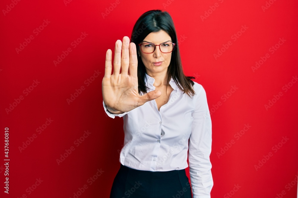 Young hispanic woman wearing business shirt and glasses doing stop sing with palm of the hand. warning expression with negative and serious gesture on the face. Young hispanic woman wearing business shirt and glasses doing stop sing with palm of the hand. warning expression with negative and serious gesture on the face.