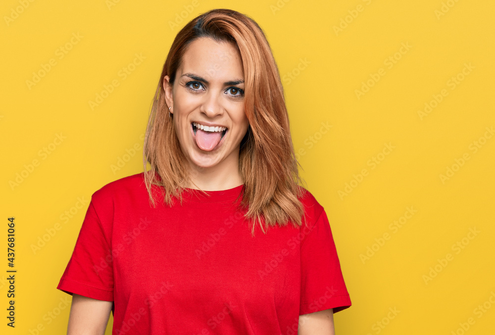 Hispanic young woman wearing casual red t shirt sticking tongue out happy with funny expression. emotion concept. Hispanic young woman wearing casual red t shirt sticking tongue out happy with funny expression. emotion concept.