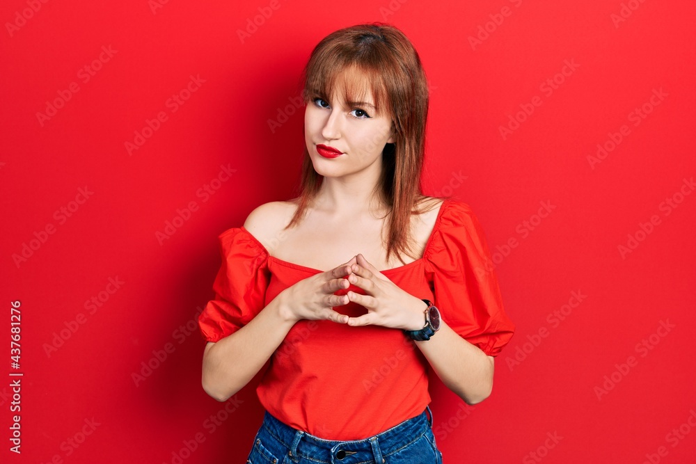 Fototapeta premium Redhead young woman wearing casual red t shirt hands together and fingers crossed smiling relaxed and cheerful. success and optimistic