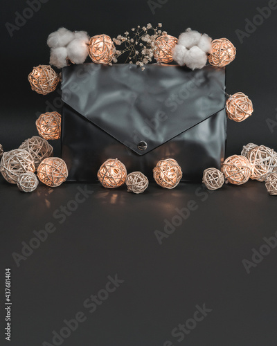 Black cosmetic bag with glowing garland of rattan balls and cotton flowers. Banner, vertical, free space for text on bottom. Instagram toning. Beauty and spa concept