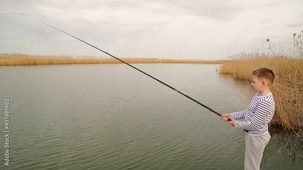 A boy in striped clothes catches a fish on fishing rod. 