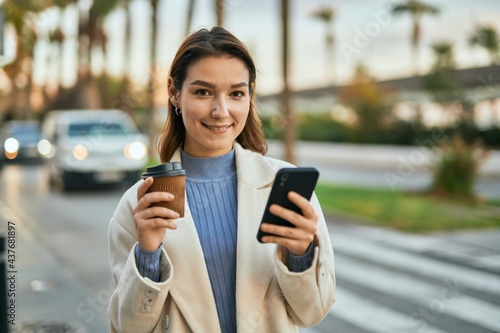 Young hispanic woman using smartphone and drinking coffee at the city.