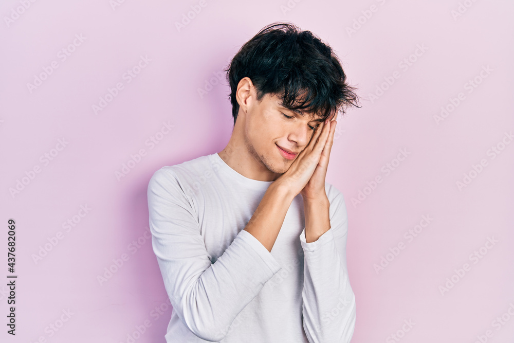 Handsome hipster young man wearing casual white shirt sleeping tired dreaming and posing with hands together while smiling with closed eyes. Handsome hipster young man wearing casual white shirt sleeping tired dreaming and posing with hands together while smiling with closed eyes.