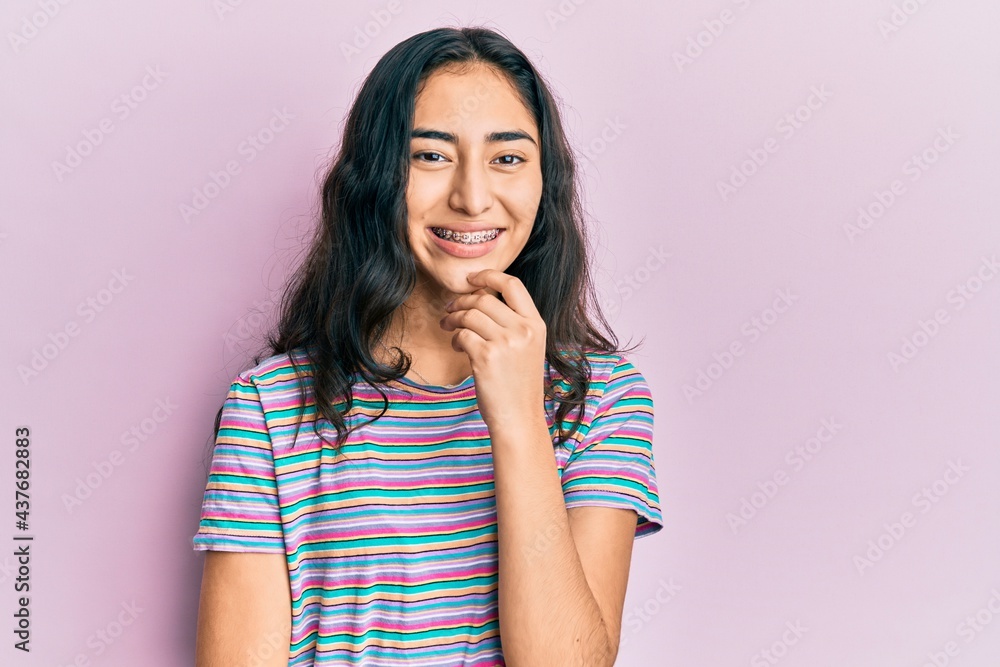Hispanic teenager girl with dental braces wearing casual clothes looking confident at the camera with smile with crossed arms and hand raised on chin. thinking positive. Hispanic teenager girl with dental braces wearing casual clothes looking confident at the camera with smile with crossed arms and hand raised on chin. thinking positive.