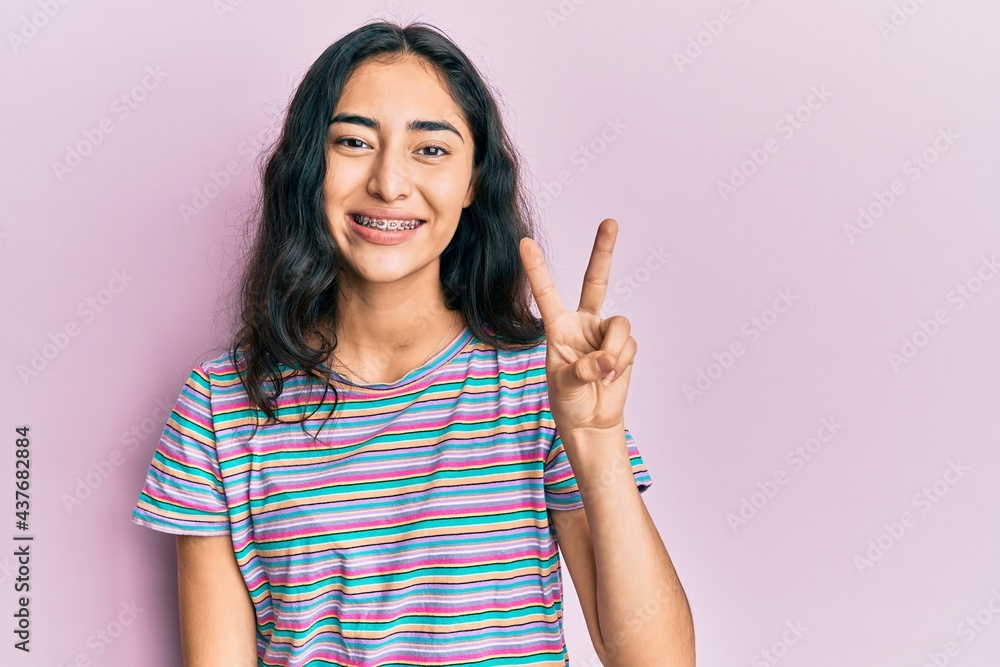 Hispanic teenager girl with dental braces wearing casual clothes showing and pointing up with fingers number two while smiling confident and happy. Hispanic teenager girl with dental braces wearing casual clothes showing and pointing up with fingers number two while smiling confident and happy.