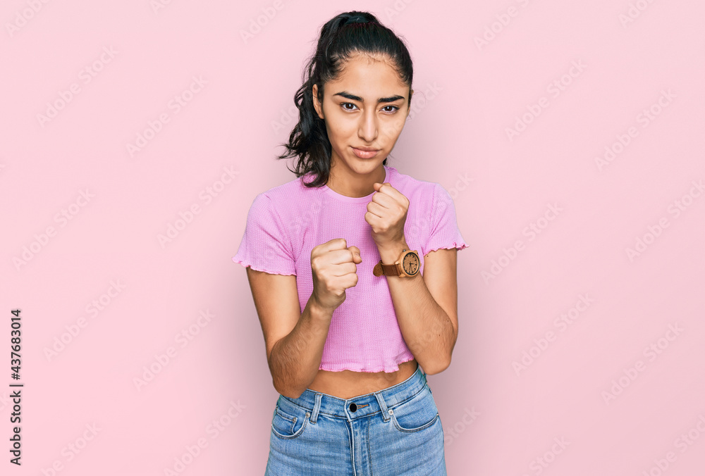 Hispanic teenager girl with dental braces wearing casual clothes ready to fight with fist defense gesture, angry and upset face, afraid of problem Hispanic teenager girl with dental braces wearing casual clothes ready to fight with fist defense gesture, angry and upset face, afraid of problem