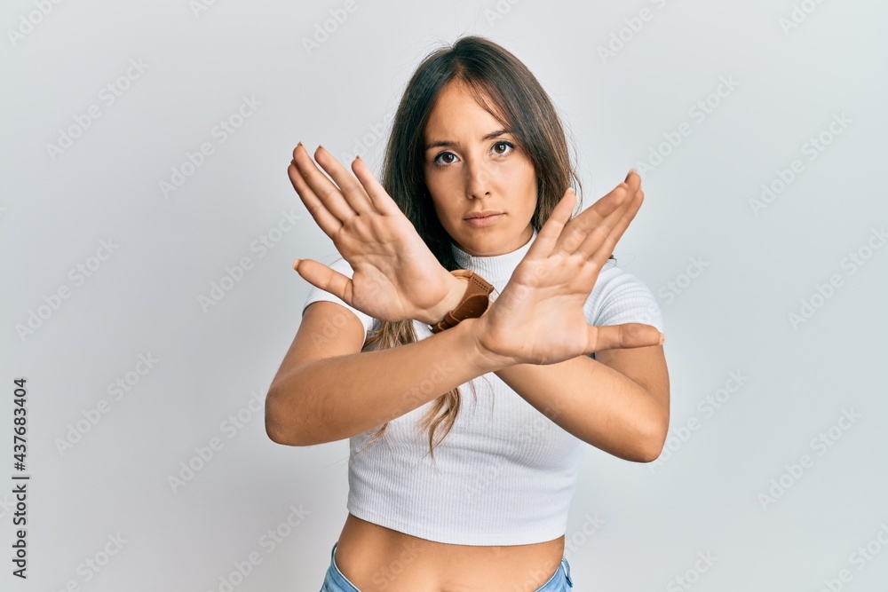 Young brunette woman wearing casual white t shirt rejection expression crossing arms doing negative sign, angry face Young brunette woman wearing casual white t shirt rejection expression crossing arms doing negative sign, angry face