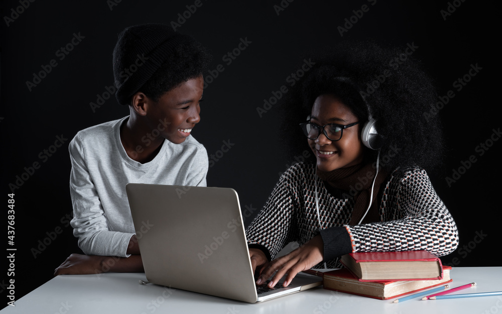 African girl wear glasses and headphones smiling at little brother while online learning with laptop textbook. Sibling student kid with sweater happy to study and cheer up each other. black background African girl wear glasses and headphones smiling at little brother while online learning with laptop textbook. Sibling student kid with sweater happy to study and cheer up each other. black background