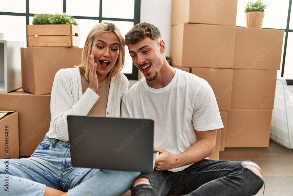 Young caucasian couple surprised using laptop sitting at new home. Young caucasian couple surprised using laptop sitting at new home.
