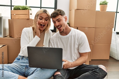 Young caucasian couple surprised using laptop sitting at new home.