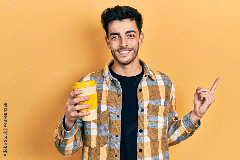 Young hispanic man holding coffee smiling happy pointing with hand and finger to the side Young hispanic man holding coffee smiling happy pointing with hand and finger to the side