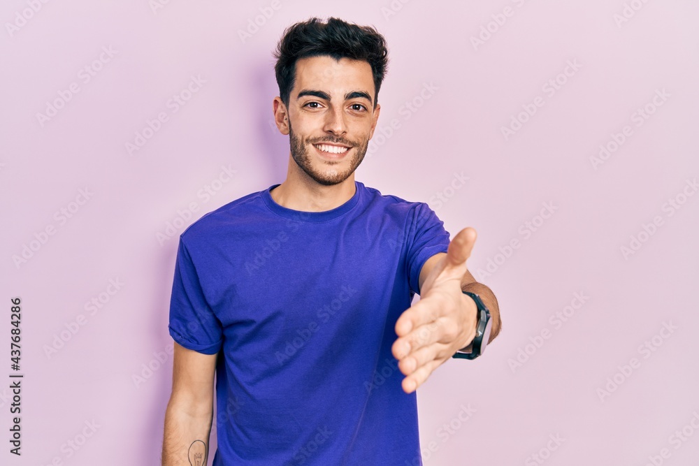 Young hispanic man wearing casual t shirt smiling friendly offering handshake as greeting and welcoming. successful business. Young hispanic man wearing casual t shirt smiling friendly offering handshake as greeting and welcoming. successful business.
