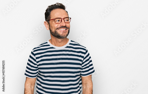 Middle age man wearing casual clothes and glasses looking away to side with smile on face, natural expression. laughing confident.