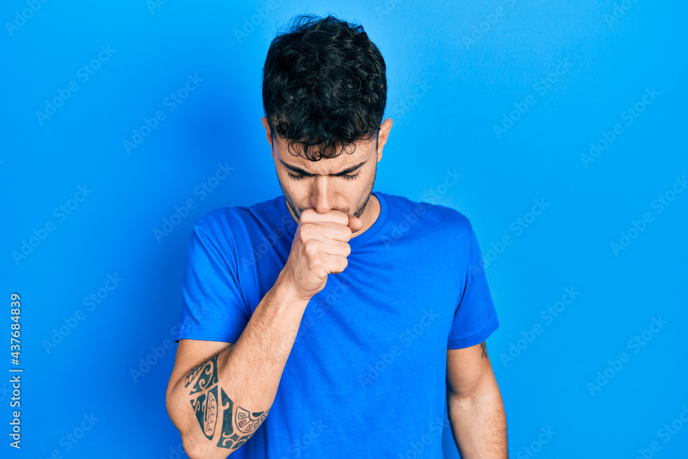Young hispanic man wearing casual blue t shirt feeling unwell and coughing as symptom for cold or bronchitis. health care concept. Young hispanic man wearing casual blue t shirt feeling unwell and coughing as symptom for cold or bronchitis. health care concept.
