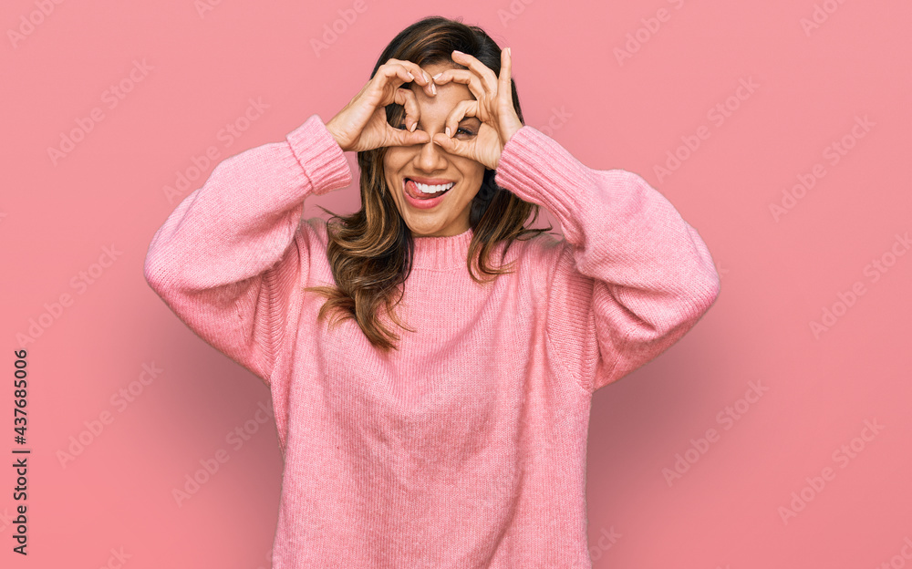 Young hispanic woman wearing casual clothes doing ok gesture like binoculars sticking tongue out, eyes looking through fingers. crazy expression. Young hispanic woman wearing casual clothes doing ok gesture like binoculars sticking tongue out, eyes looking through fingers. crazy expression.