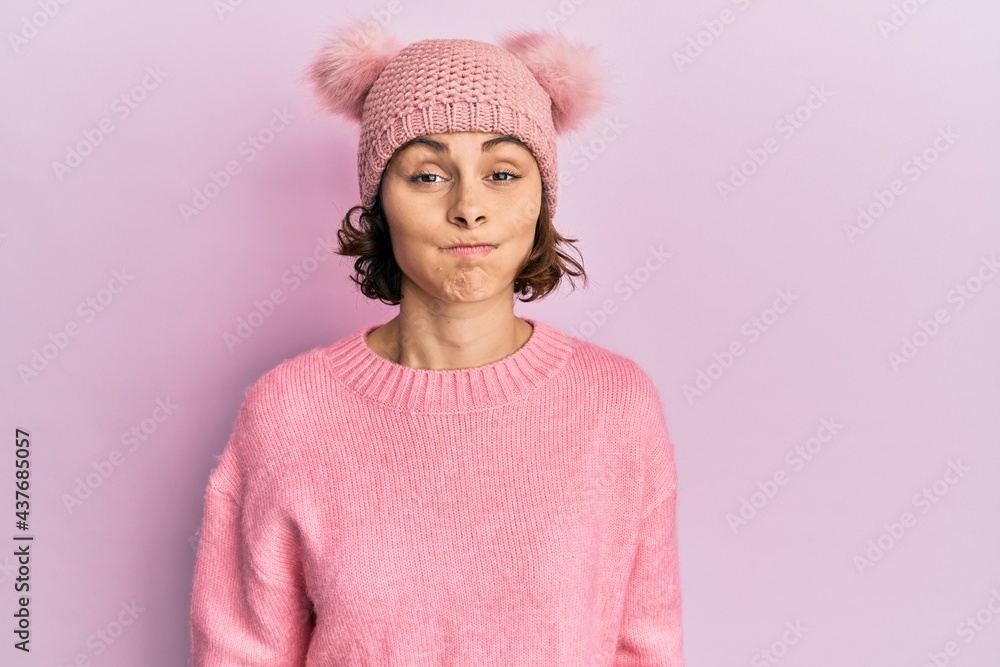 Young brunette woman wearing cute wool cap puffing cheeks with funny face. mouth inflated with air, crazy expression. Young brunette woman wearing cute wool cap puffing cheeks with funny face. mouth inflated with air, crazy expression.