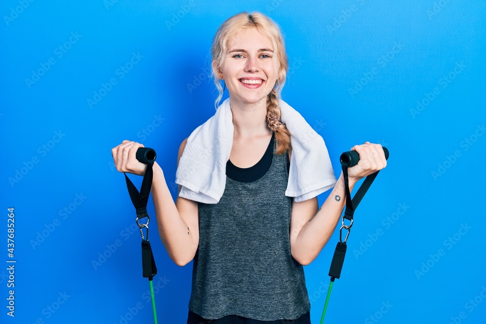 Beautiful caucasian sports woman with blond hair training arm resistance with elastic arm bands smiling with a happy and cool smile on face. showing teeth.