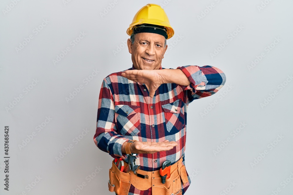 Senior hispanic man wearing handyman uniform gesturing with hands showing big and large size sign, measure symbol. smiling looking at the camera. measuring concept. Senior hispanic man wearing handyman uniform gesturing with hands showing big and large size sign, measure symbol. smiling looking at the camera. measuring concept.