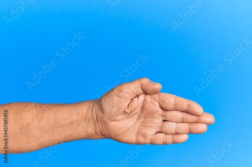 Hand of senior hispanic man over blue isolated background stretching and reaching with open hand for handshake, showing palm