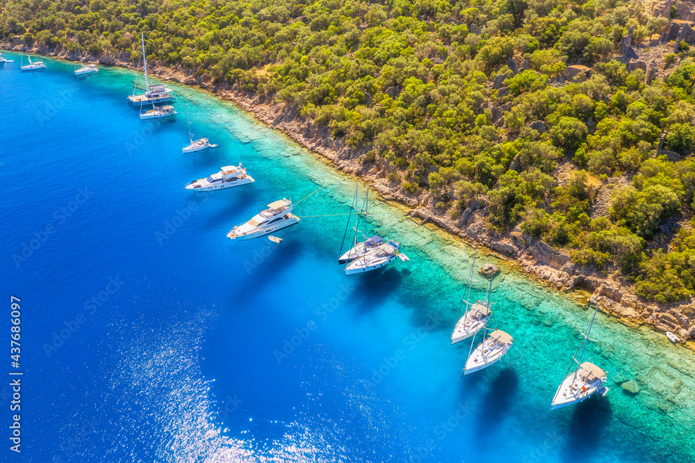 Aerial view of beautiful yachts and boats on the sea bay at sunset in summer. Gemiler Island in Turkey. Top view of luxury yachts, sailboats, clear blue water, beach, mountain and green forest. Nature