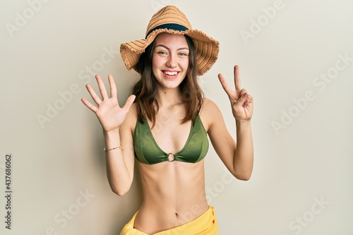 Young brunette woman wearing bikini showing and pointing up with fingers number seven while smiling confident and happy.