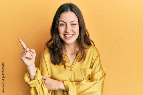 Young brunette woman wearing casual yellow shirt smiling happy pointing with hand and finger to the side