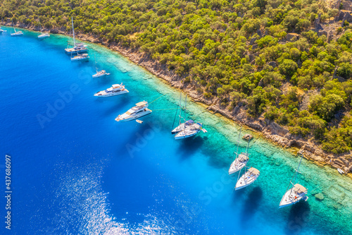 Aerial view of beautiful yachts and boats on the sea bay at sunset in summer. Gemiler Island in Turkey. Top view of luxury yachts, sailboats, clear blue water, beach, mountain and green forest. Nature