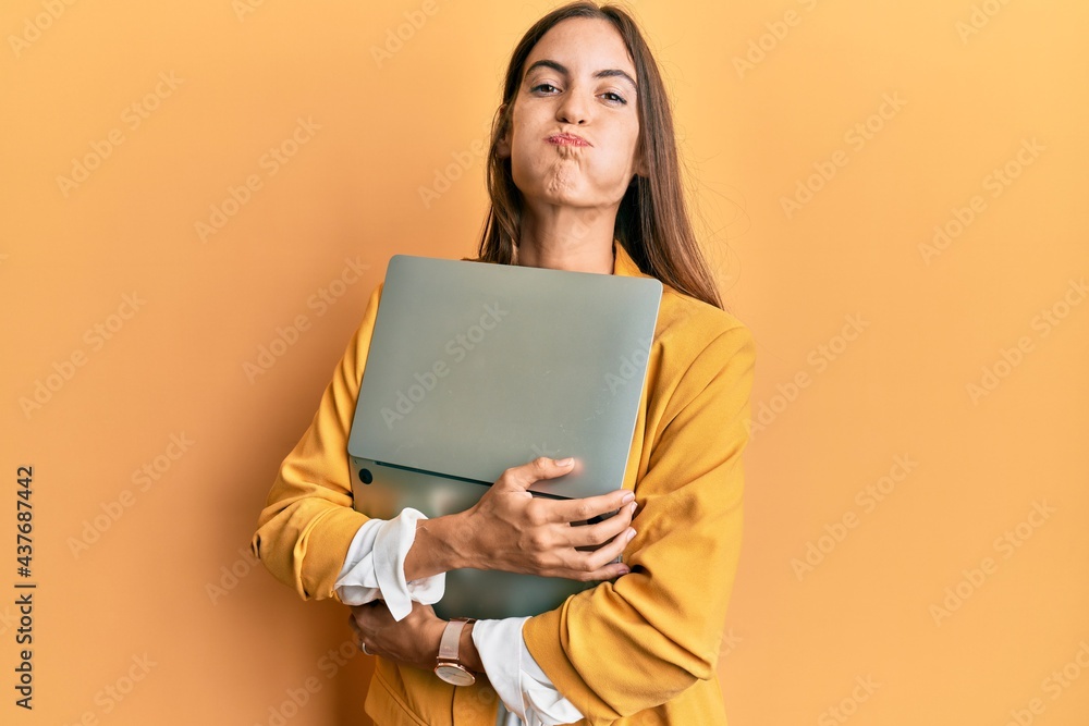 Young beautiful woman holding laptop puffing cheeks with funny face. mouth inflated with air, catching air. Young beautiful woman holding laptop puffing cheeks with funny face. mouth inflated with air, catching air.