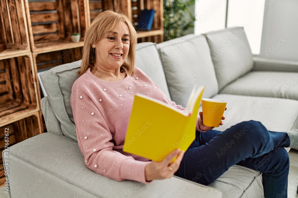 Middle age blonde woman smiling happy reading book and drinking coffee at home. Middle age blonde woman smiling happy reading book and drinking coffee at home.