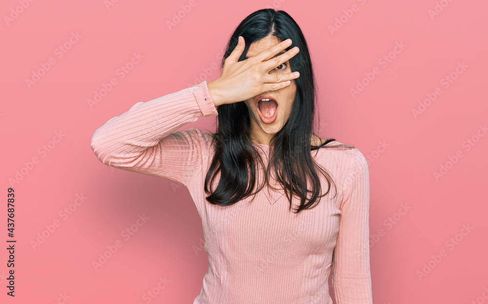 Young hispanic woman wearing casual clothes peeking in shock covering face and eyes with hand, looking through fingers with embarrassed expression. Young hispanic woman wearing casual clothes peeking in shock covering face and eyes with hand, looking through fingers with embarrassed expression.
