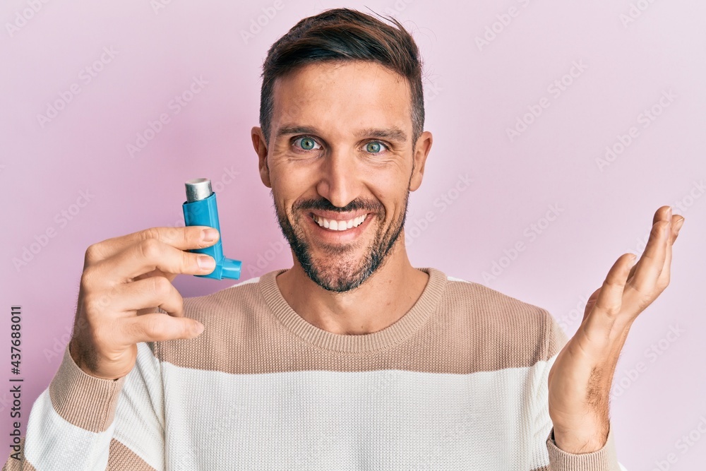 Handsome man with beard holding medical asthma inhaler celebrating achievement with happy smile and winner expression with raised hand Handsome man with beard holding medical asthma inhaler celebrating achievement with happy smile and winner expression with raised hand