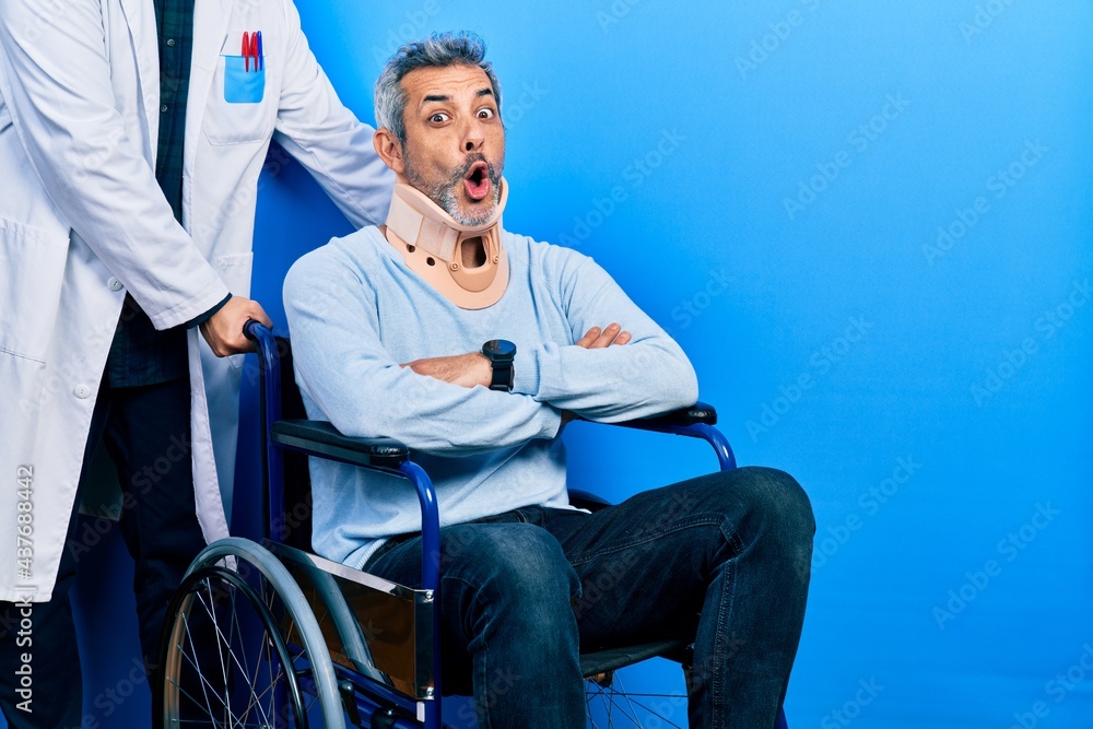 Handsome middle age man with grey hair on wheelchair wearing cervical collar afraid and shocked with surprise expression, fear and excited face.