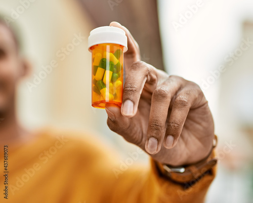 Young african american man smiling happy holding pills at the city.