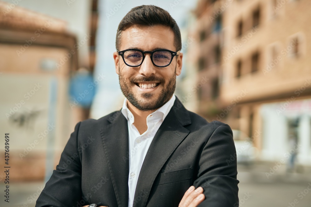 Fototapeta premium Young hispanic businessman with arms crossed smiling happy at the city.