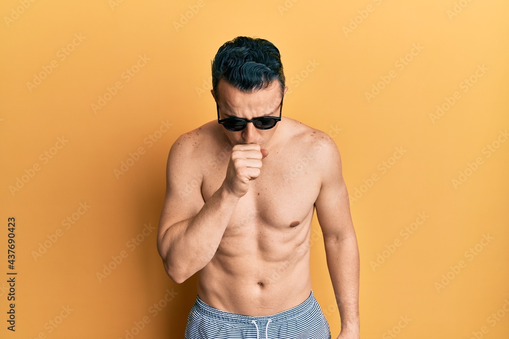 Handsome young man wearing swimsuit and sunglasses feeling unwell and coughing as symptom for cold or bronchitis. health care concept.