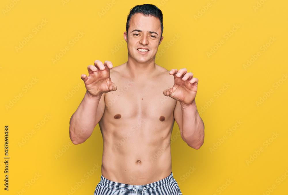 Handsome young man wearing swimwear shirtless smiling funny doing claw gesture as cat, aggressive and sexy expression
