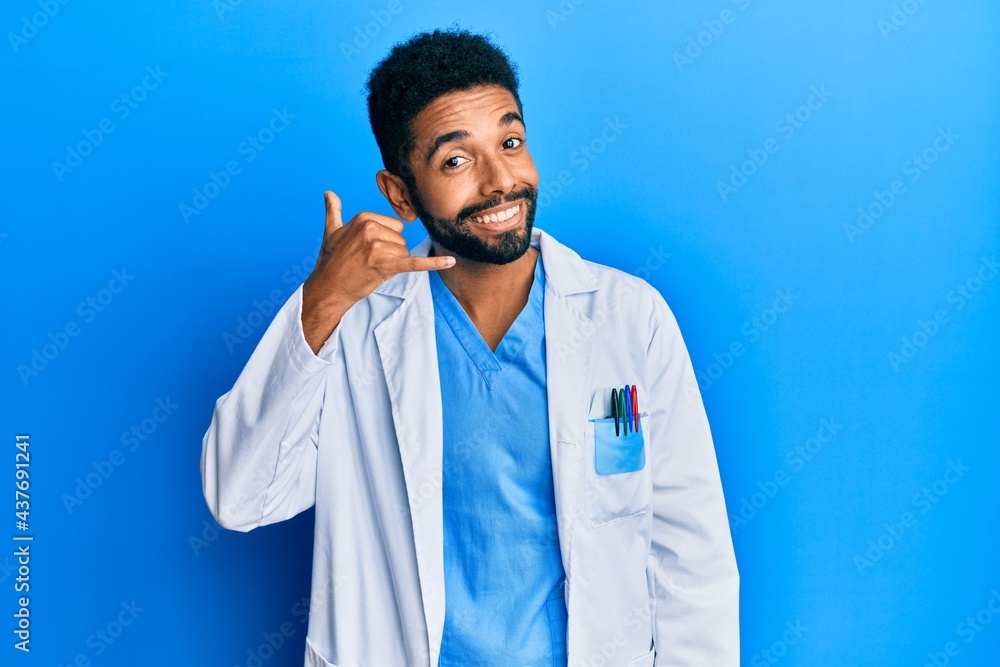 Handsome hispanic man with beard wearing doctor uniform smiling doing phone gesture with hand and fingers like talking on the telephone. communicating concepts. Handsome hispanic man with beard wearing doctor uniform smiling doing phone gesture with hand and fingers like talking on the telephone. communicating concepts.