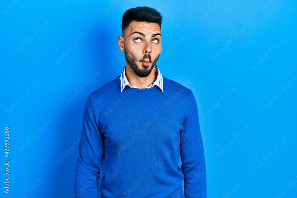 Young hispanic man with beard wearing casual blue sweater making fish face with lips, crazy and comical gesture. funny expression. Young hispanic man with beard wearing casual blue sweater making fish face with lips, crazy and comical gesture. funny expression.