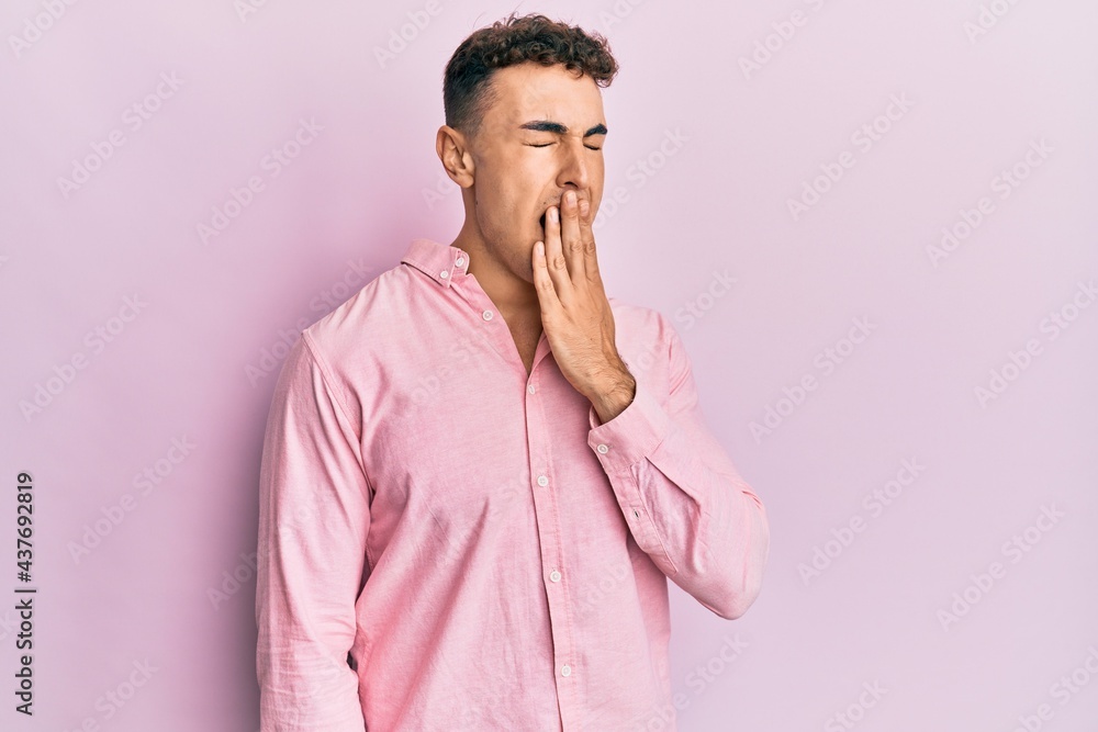 Hispanic young man wearing casual clothes bored yawning tired covering mouth with hand. restless and sleepiness. Hispanic young man wearing casual clothes bored yawning tired covering mouth with hand. restless and sleepiness.