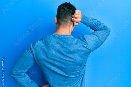 Hispanic young man wearing casual winter sweater backwards thinking about doubt with hand on head