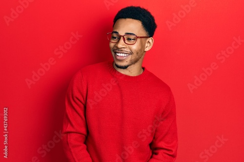 Young african american man wearing casual clothes and glasses looking away to side with smile on face, natural expression. laughing confident. © Krakenimages.com