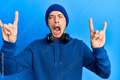 Hispanic young man wearing sweatshirt and headphones shouting with crazy expression doing rock symbol with hands up. music star. heavy concept.