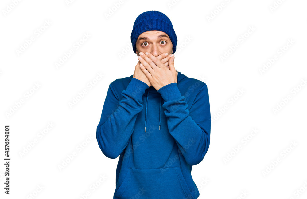 Hispanic young man wearing sweatshirt and wool hat shocked covering mouth with hands for mistake. secret concept. Hispanic young man wearing sweatshirt and wool hat shocked covering mouth with hands for mistake. secret concept.