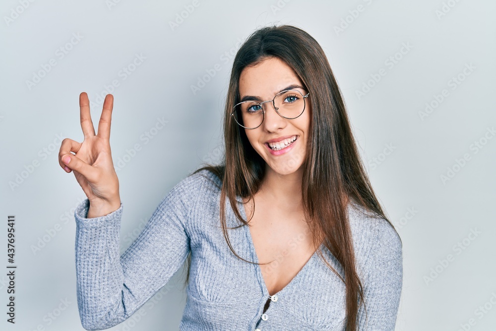Young brunette teenager wearing casual sweater and glasses showing and pointing up with fingers number two while smiling confident and happy. Young brunette teenager wearing casual sweater and glasses showing and pointing up with fingers number two while smiling confident and happy.