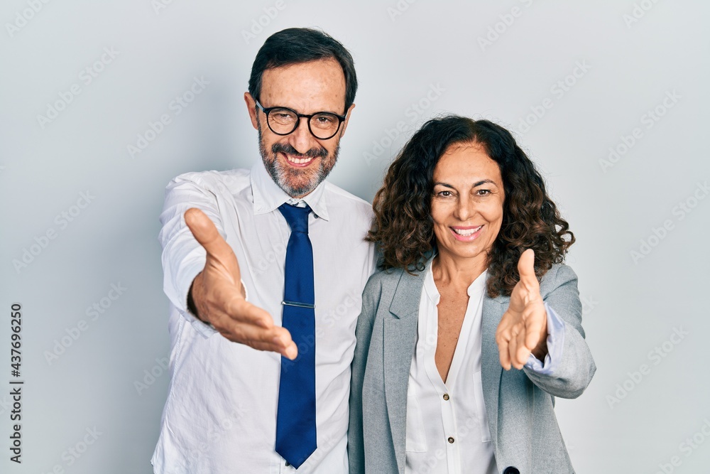 Middle age couple of hispanic woman and man wearing business office uniform smiling friendly offering handshake as greeting and welcoming. successful business. Middle age couple of hispanic woman and man wearing business office uniform smiling friendly offering handshake as greeting and welcoming. successful business.