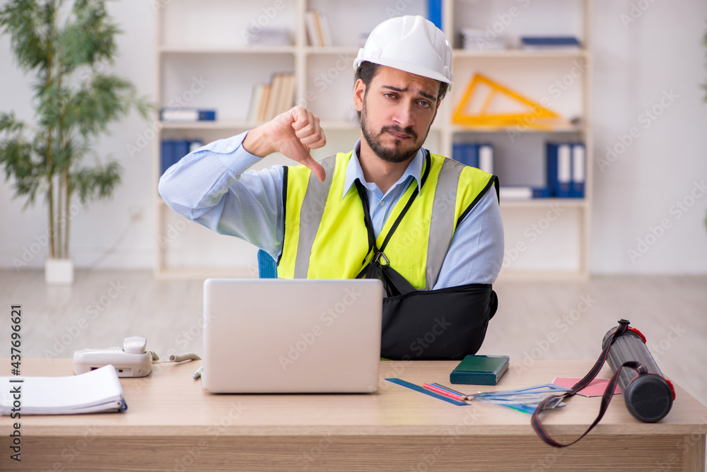 Young arm injured male architect working in the office Young arm injured male architect working in the office