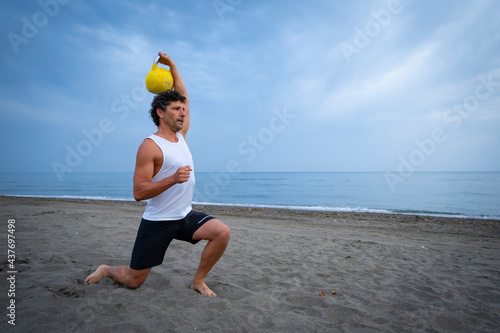 Male athlete exercising at the beach with kettle bells photo