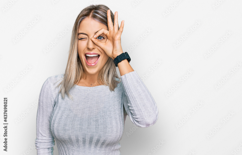 Beautiful blonde woman wearing casual clothes doing ok gesture with hand smiling, eye looking through fingers with happy face. Beautiful blonde woman wearing casual clothes doing ok gesture with hand smiling, eye looking through fingers with happy face.